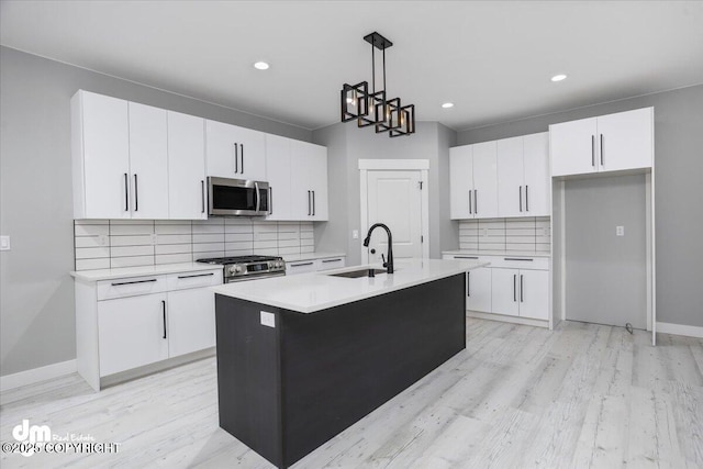 kitchen with appliances with stainless steel finishes, a sink, white cabinets, backsplash, and light wood-type flooring