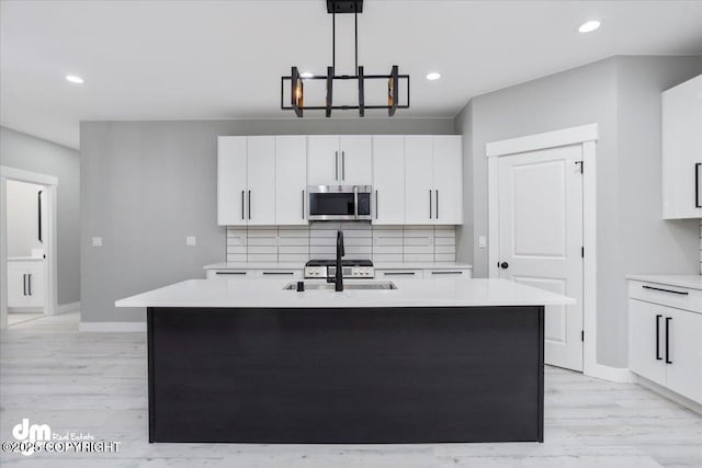 kitchen with stainless steel microwave, light countertops, backsplash, light wood-style floors, and recessed lighting