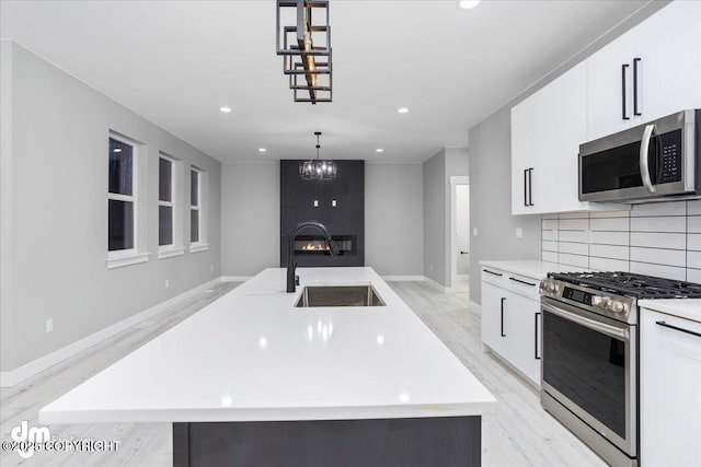 kitchen featuring appliances with stainless steel finishes, light wood-style flooring, a sink, a fireplace, and a chandelier