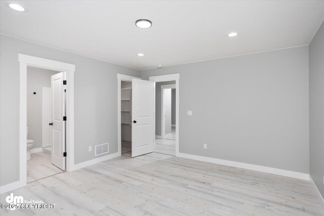 unfurnished bedroom featuring wood finished floors, baseboards, a walk in closet, a closet, and recessed lighting