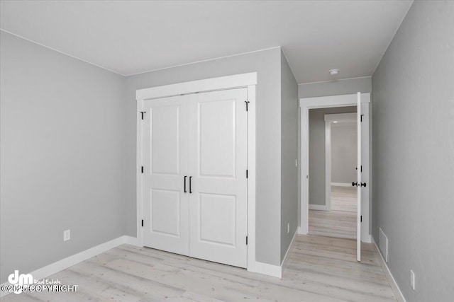 unfurnished bedroom with light wood-type flooring, a closet, and baseboards