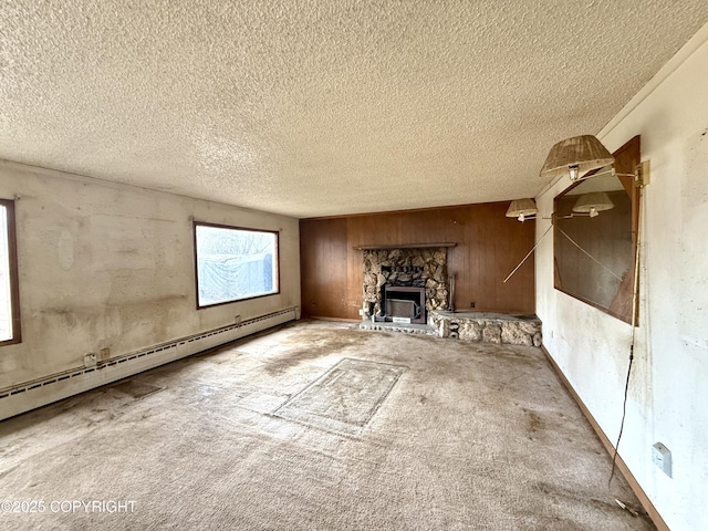 unfurnished living room featuring baseboard heating, a textured ceiling, carpet, wood walls, and a stone fireplace