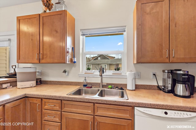 kitchen featuring dishwasher, a sink, light countertops, and brown cabinetry
