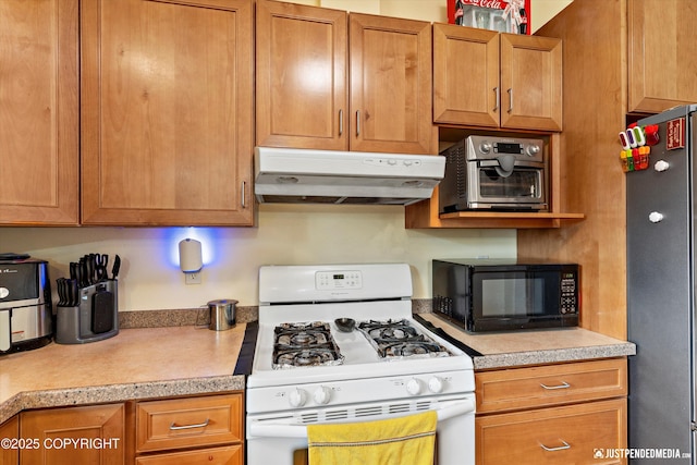 kitchen with white range with gas stovetop, under cabinet range hood, freestanding refrigerator, black microwave, and light countertops