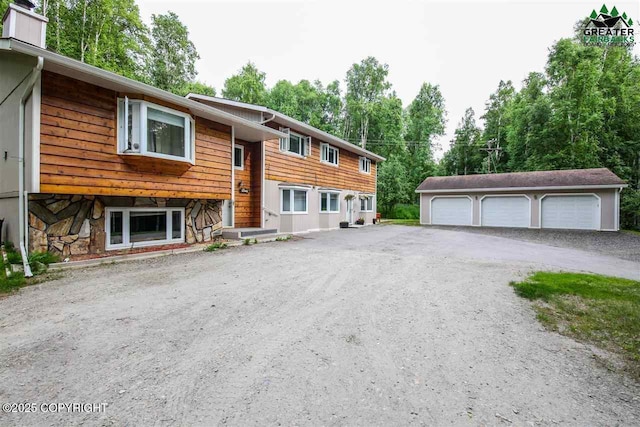 bi-level home featuring stone siding, an outbuilding, and a garage