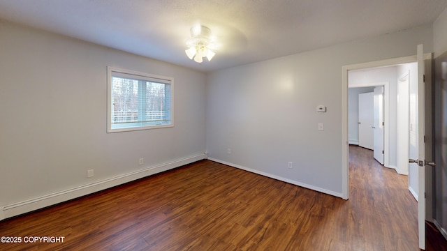 empty room featuring a baseboard heating unit, baseboards, and wood finished floors