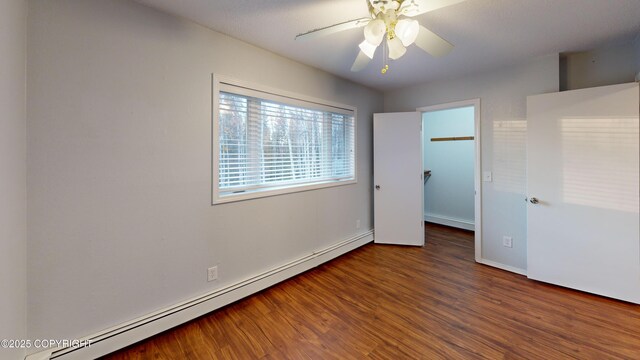 unfurnished bedroom with wood finished floors, a ceiling fan, baseboards, baseboard heating, and a spacious closet
