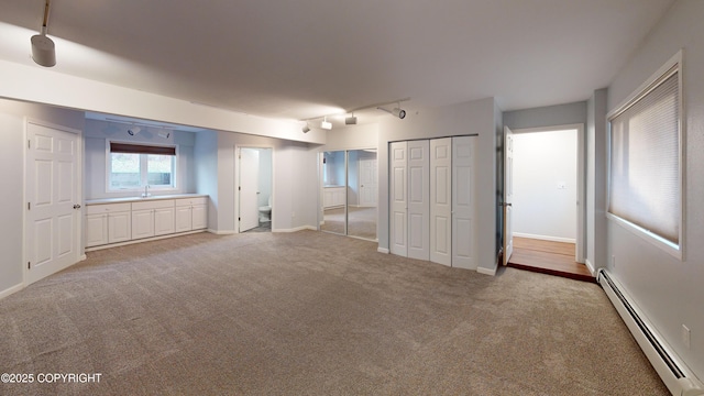 unfurnished bedroom with track lighting, two closets, light carpet, baseboard heating, and baseboards