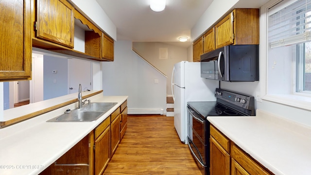 kitchen featuring a sink, a baseboard radiator, light wood finished floors, light countertops, and electric range