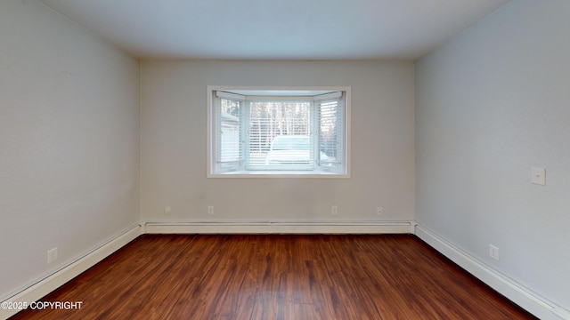 spare room featuring baseboards, baseboard heating, and dark wood-style floors