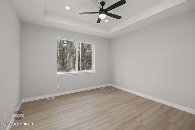 unfurnished room with a tray ceiling, recessed lighting, light wood-style floors, ceiling fan, and baseboards