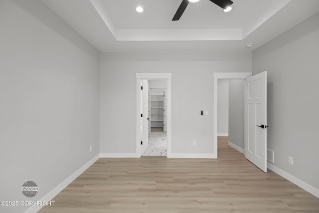 unfurnished bedroom with a raised ceiling, light wood-style floors, baseboards, recessed lighting, and a ceiling fan