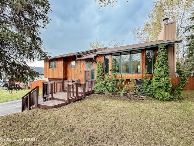 back of house with a chimney, a wooden deck, and a lawn