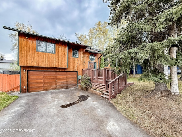 rustic home with driveway, a deck, fence, and an attached garage