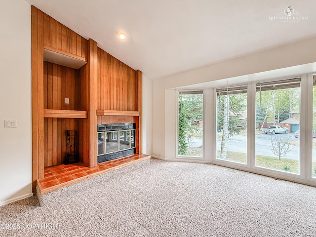 unfurnished living room with lofted ceiling, healthy amount of natural light, carpet, wood walls, and a tiled fireplace
