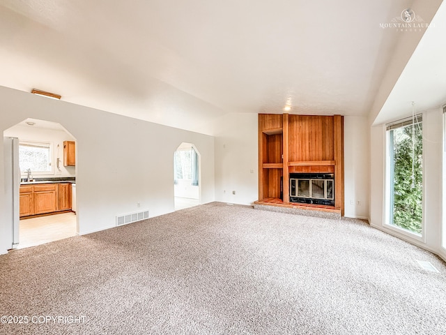 unfurnished living room featuring lofted ceiling, light colored carpet, a fireplace, and healthy amount of natural light
