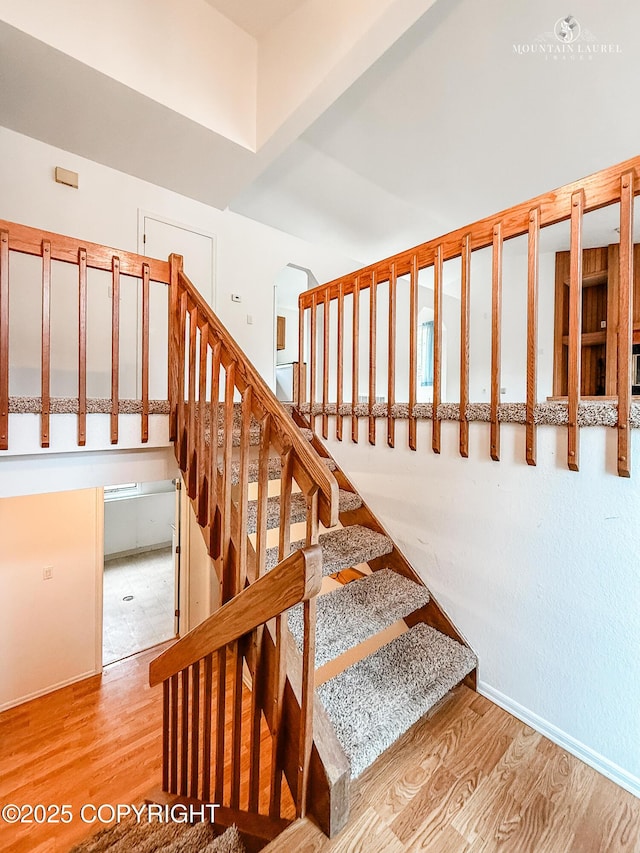 stairway with wood finished floors, arched walkways, and baseboards