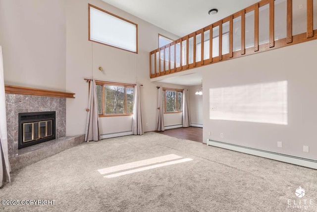 unfurnished living room with a high end fireplace, a towering ceiling, a baseboard radiator, carpet flooring, and a notable chandelier