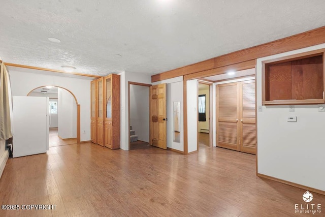 spare room featuring a textured ceiling, stairway, light wood finished floors, a baseboard radiator, and arched walkways