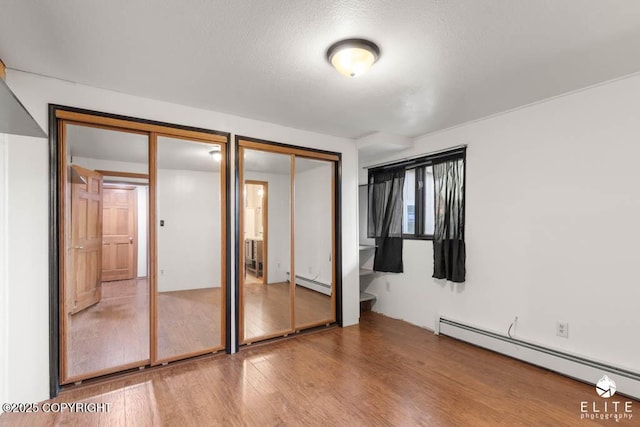 unfurnished bedroom with a textured ceiling, wood finished floors, multiple closets, and a baseboard heating unit