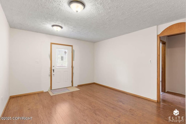 interior space with baseboards, arched walkways, a textured ceiling, and wood finished floors