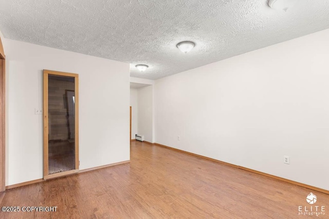 empty room with a textured ceiling, wood finished floors, baseboards, and a baseboard heating unit