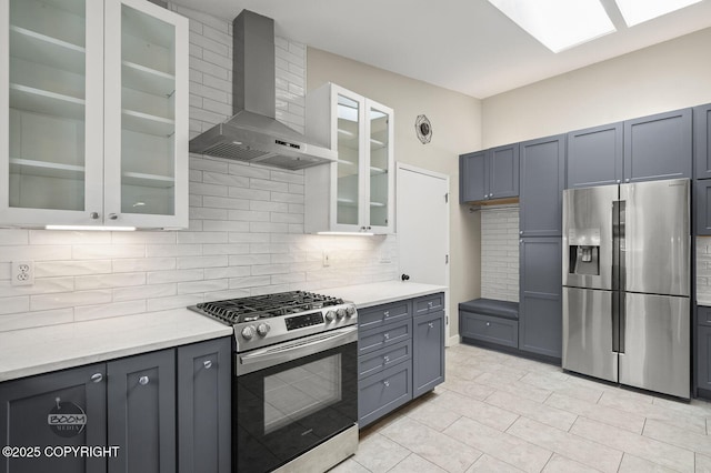 2563 La Honda Dr, Anchorage, AK 99517 - kitchen featuring stainless steel appliances, wall chimney range hood, tasteful backsplash, light countertops, and glass insert cabinets