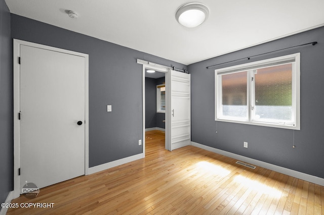 2563 La Honda Dr, Anchorage, AK 99517 - unfurnished bedroom featuring light wood-style floors, a barn door, and baseboards