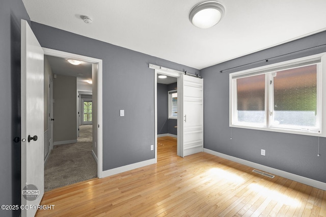2563 La Honda Dr, Anchorage, AK 99517 - unfurnished bedroom with a barn door, light wood-style floors, and baseboards