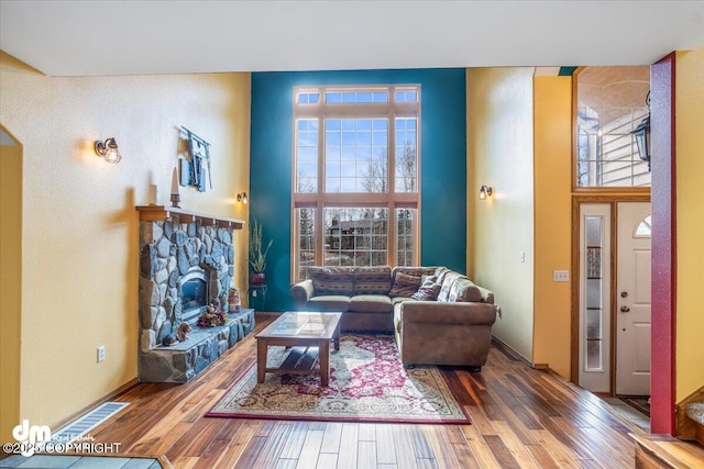 living area with a fireplace, a towering ceiling, and wood finished floors