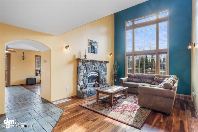 living area with wood finished floors, a high ceiling, a fireplace, baseboards, and arched walkways