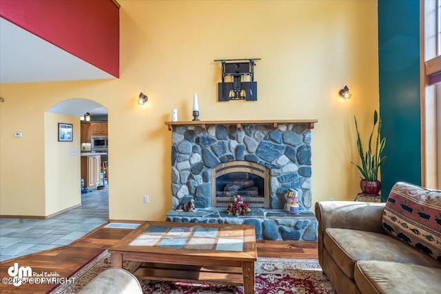 tiled living area featuring baseboards, a fireplace, a towering ceiling, and arched walkways