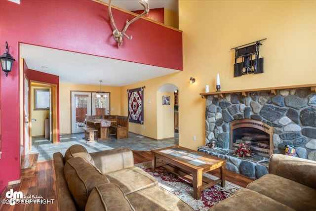 living room with arched walkways, a stone fireplace, and wood finished floors