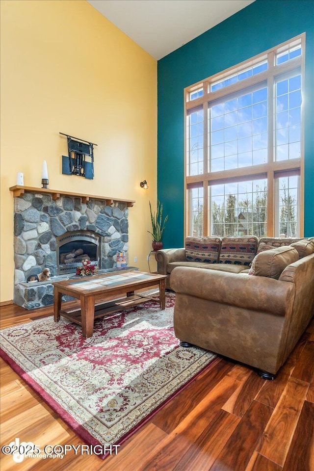 living room featuring a stone fireplace, a towering ceiling, and wood finished floors