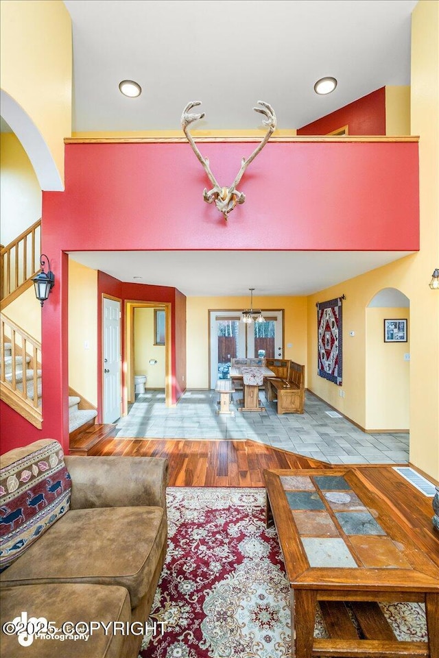 living room featuring wood finished floors, stairs, arched walkways, a chandelier, and recessed lighting