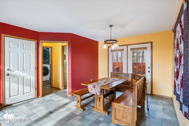 dining room featuring an inviting chandelier, stacked washer and clothes dryer, and baseboards