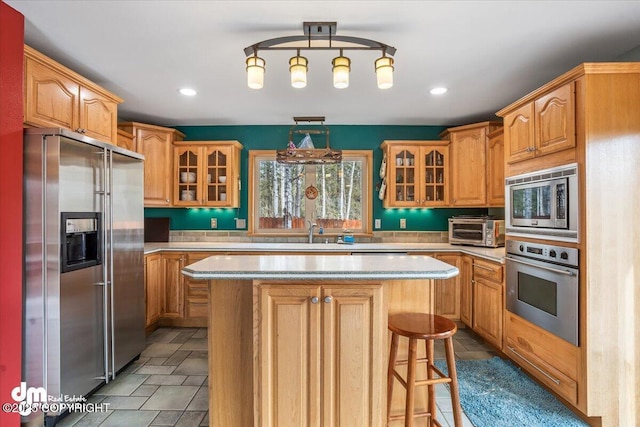 kitchen with a sink, stainless steel appliances, a kitchen bar, glass insert cabinets, and a kitchen island