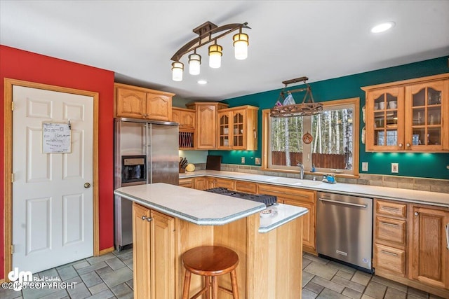 kitchen featuring a sink, light countertops, glass insert cabinets, a kitchen island, and appliances with stainless steel finishes