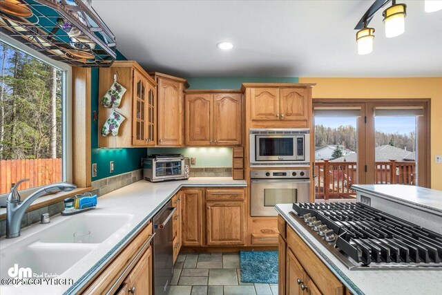 kitchen with light countertops, appliances with stainless steel finishes, glass insert cabinets, and a sink