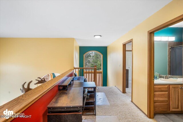 hallway featuring a sink, light colored carpet, and an upstairs landing