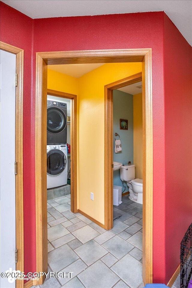 hallway with stacked washing maching and dryer, baseboards, and light tile patterned floors