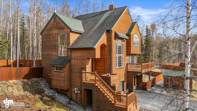 view of front of home featuring fence, a deck, stairway, a chimney, and a shingled roof