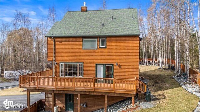 rear view of property featuring a shingled roof, a yard, a chimney, and a deck