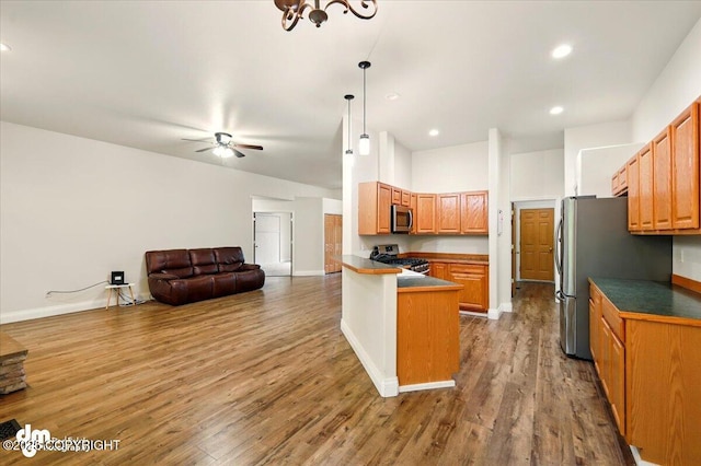 kitchen with appliances with stainless steel finishes, dark countertops, a peninsula, a ceiling fan, and open floor plan