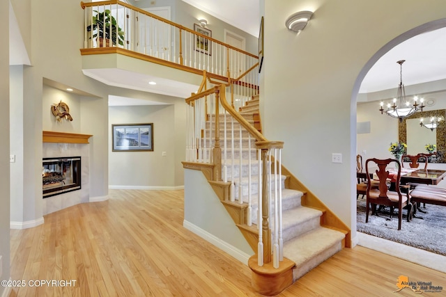 stairs with arched walkways, wood finished floors, a chandelier, a multi sided fireplace, and baseboards