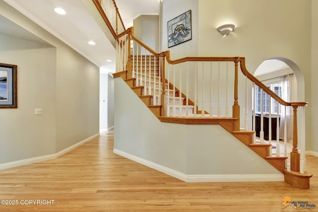 staircase featuring wood finished floors, baseboards, recessed lighting, ornamental molding, and arched walkways