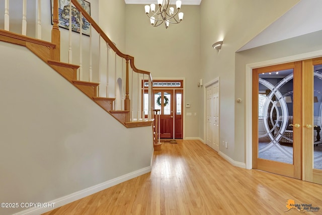 foyer entrance featuring wood finished floors, a chandelier, baseboards, stairs, and french doors