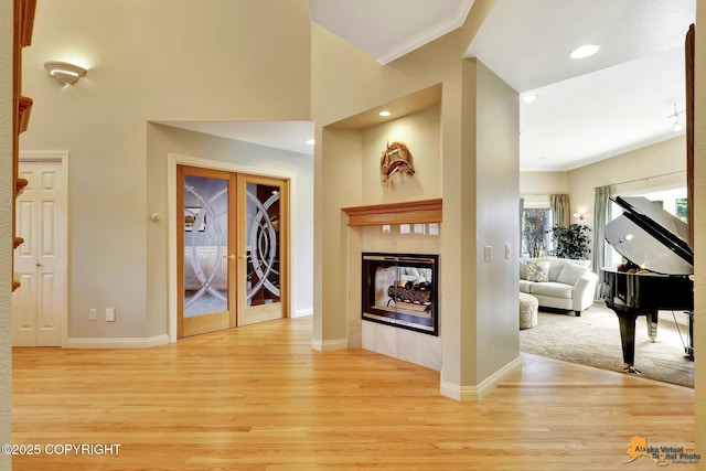 living area with french doors, light wood-style floors, ornamental molding, baseboards, and a multi sided fireplace