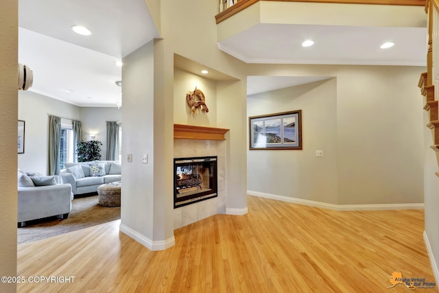 living room featuring a tiled fireplace, light wood-style flooring, ornamental molding, baseboards, and recessed lighting