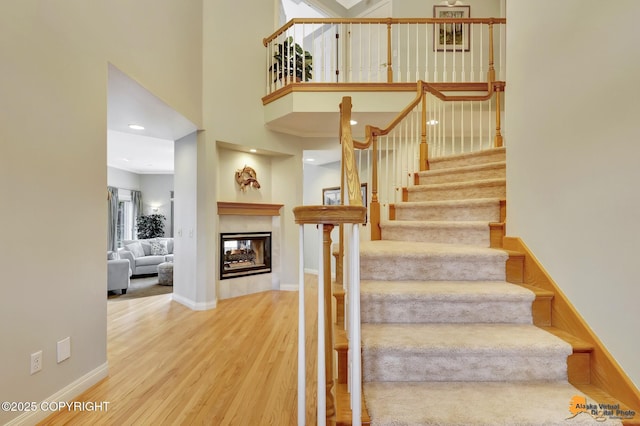 stairs featuring wood finished floors, a multi sided fireplace, baseboards, and a high ceiling